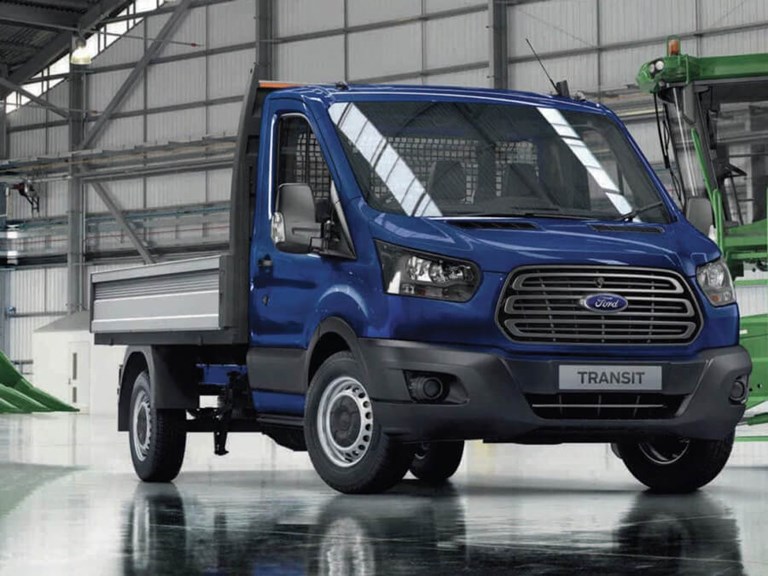 Brand new, flat-backed blue Ford transit van in large warehouse, available to hire.